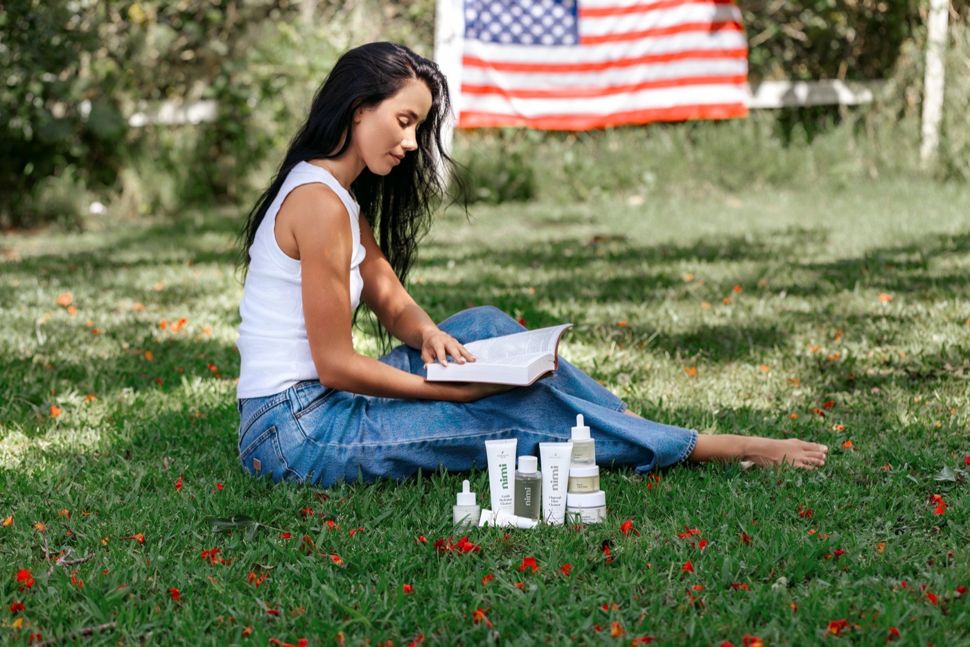 A woman relaxing on the grass with Nimi Skincare products and an American flag, proudly made in America